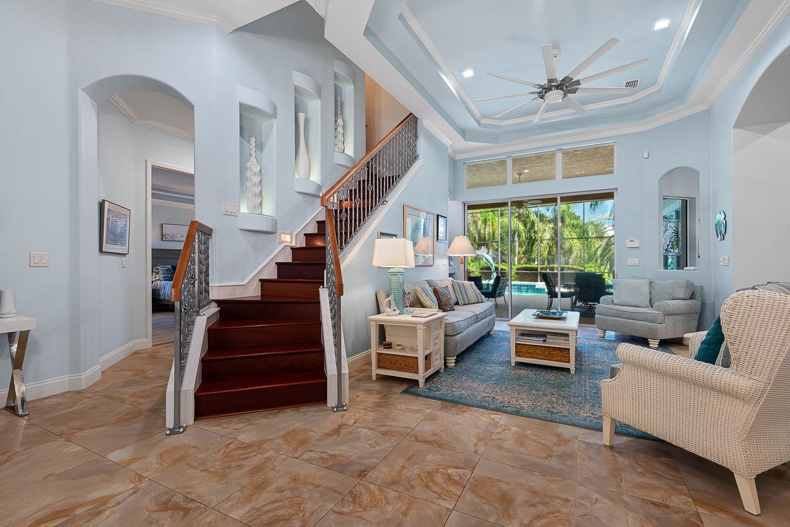Grand two-story foyer with tray ceiling, custom staircase, and sliding-glass view to the pool lanai