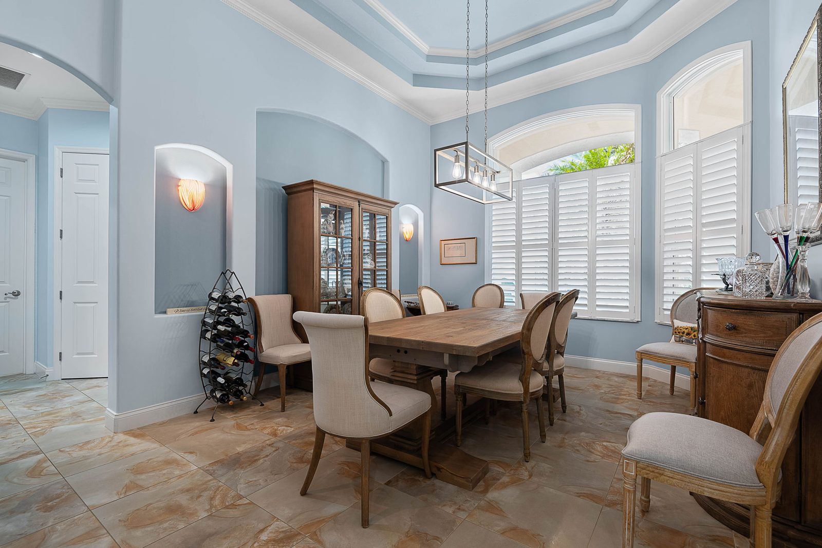 Formal dining room with tray ceiling, arched windows, and plantation shutters