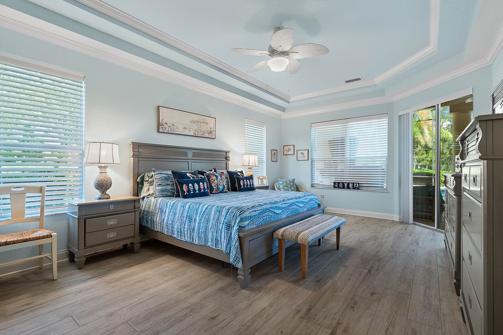 Primary bedroom suite with tray ceiling, wood-look tile flooring, and private lanai access